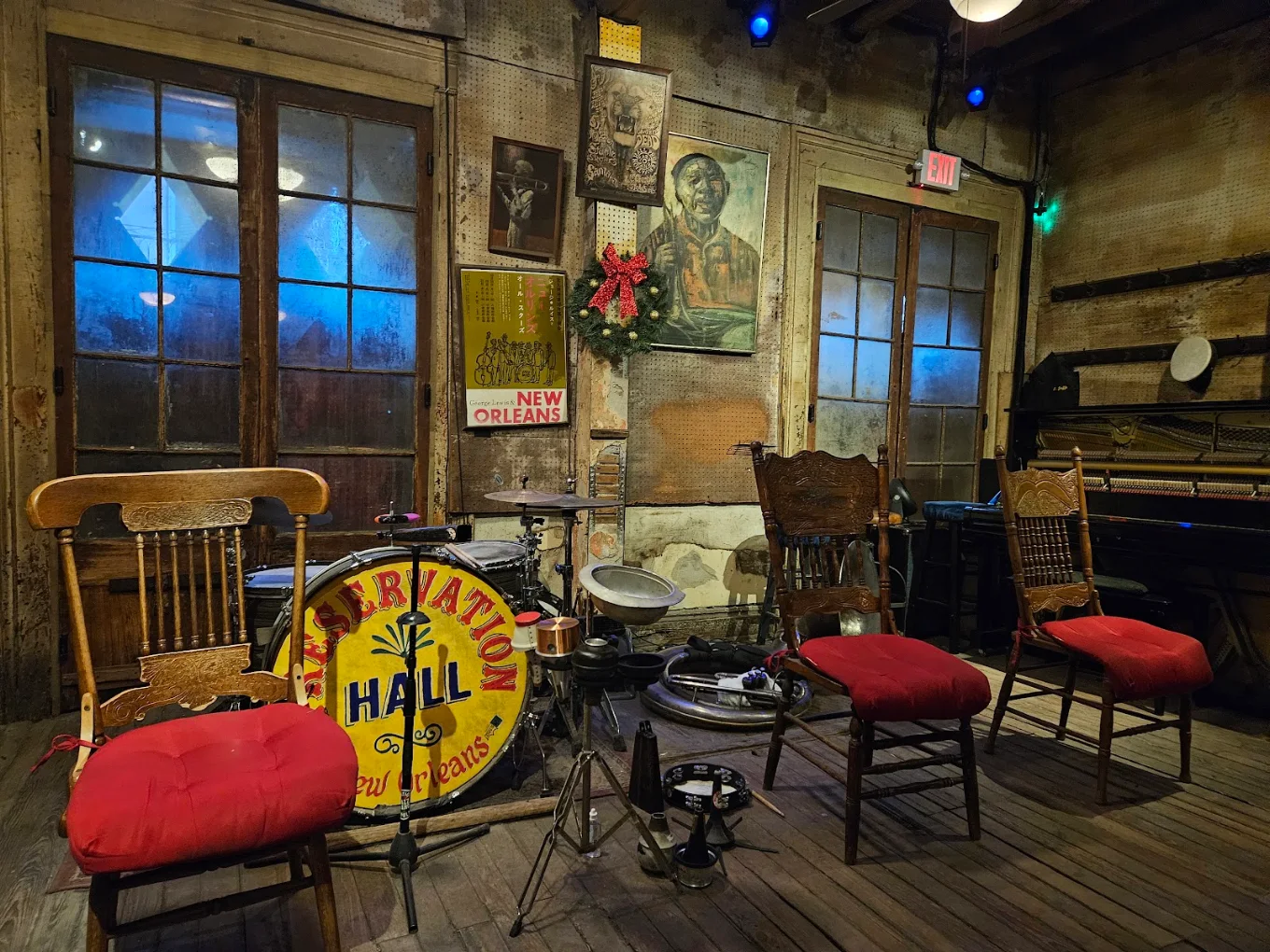 A cozy lounge with a drum set, piano, and wooden chairs.