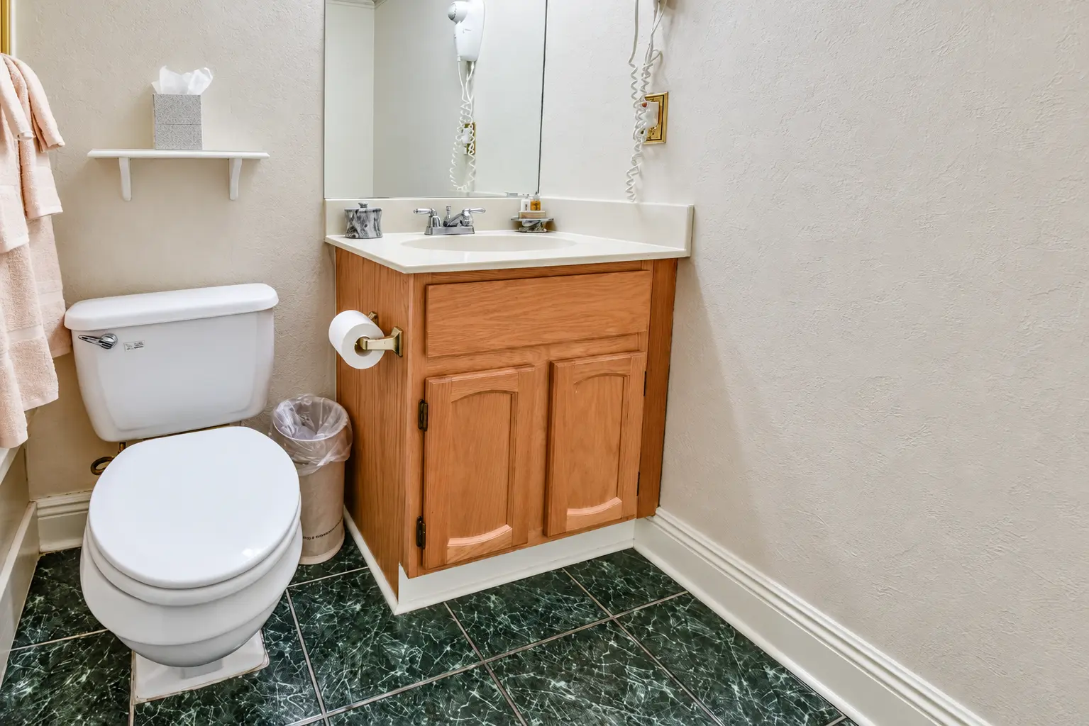 Guest bathroom with wooden vanity, large mirror, and green tile flooring at Plaza Suite Resort in New Orleans