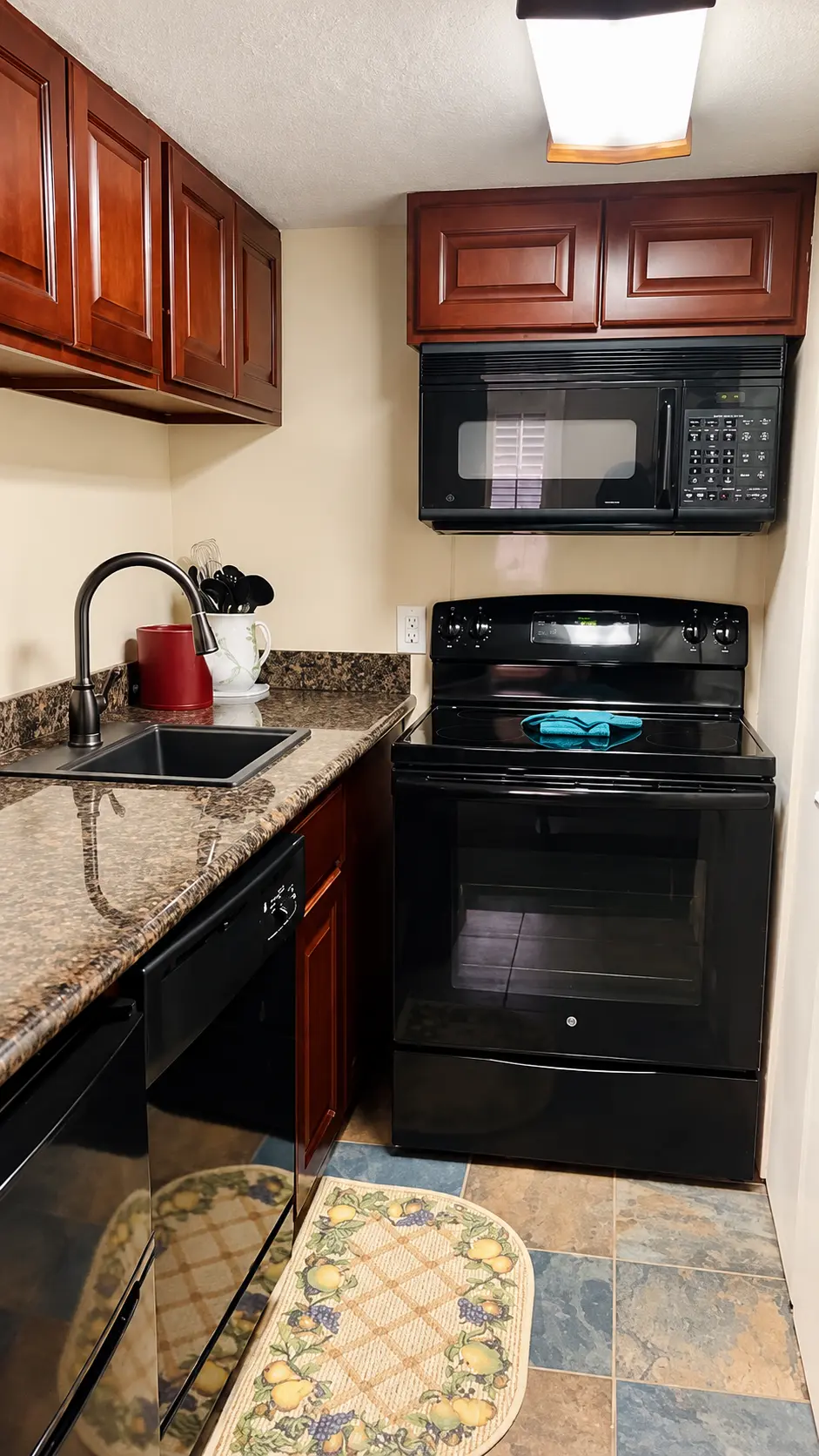 Studio suite kitchenette with wood cabinets, stove, microwave, and dishwasher at Plaza Suite Resort in New Orleans