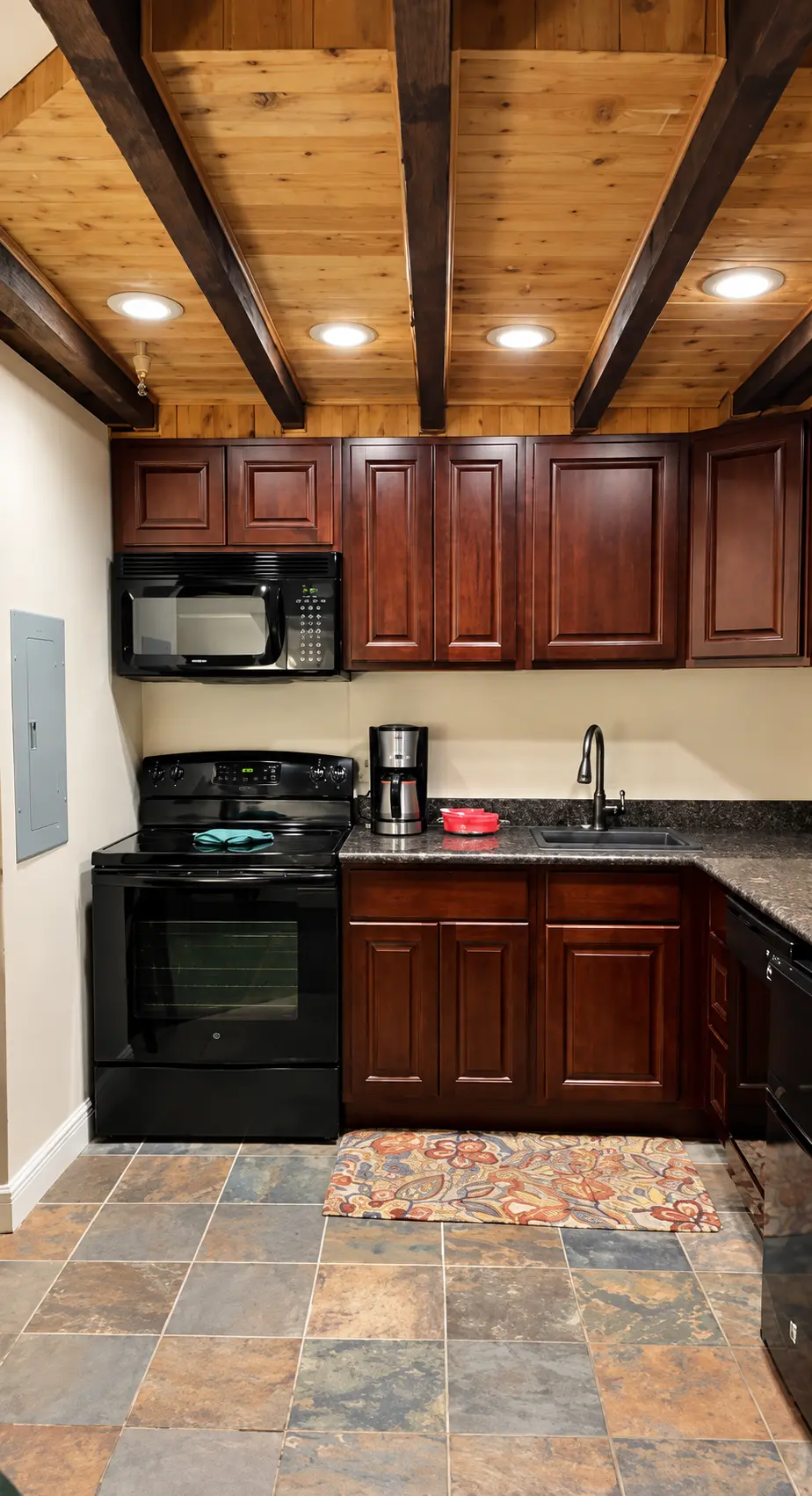 Suite kitchenette with wood cabinets, exposed ceiling beams, stove, and microwave at Plaza Suite Resort in New Orleans